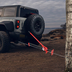Farm jack attached to a tree with a chain, near a car