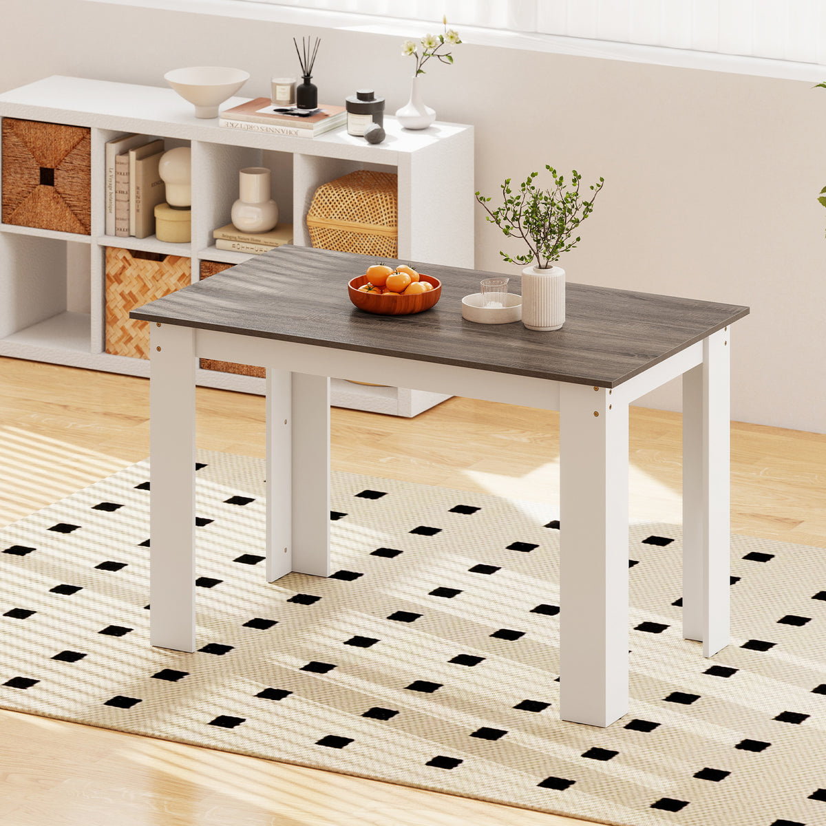 The dining table shown on a rug with a shelf unit in the background