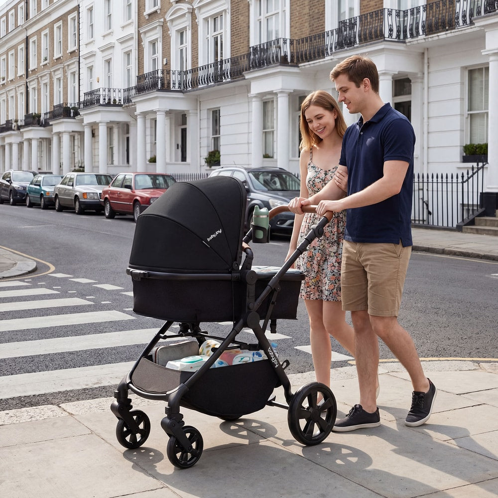 The baby stroller in bassinet mode being pushed by a couple on a city pavement