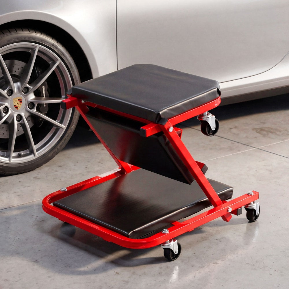 Red rolling creeper seat garage chair with black padding parked next to a car wheel