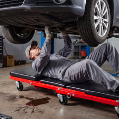 Mechanic lying on a red rolling creeper seat garage chair under a car