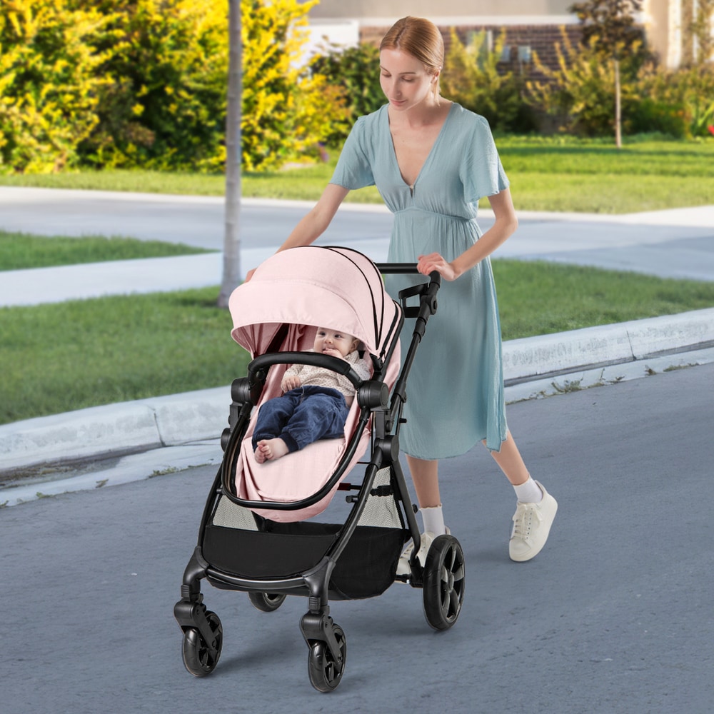 A woman pushing a pink convertible baby stroller with a baby inside down a street