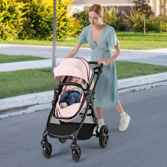 A woman pushing a pink convertible baby stroller with a baby inside down a street