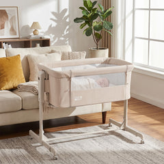 Beige bedside crib with a baby sleeping inside, positioned next to a sofa