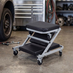 The mechanic seat in its folded position sitting on a concrete garage floor near a car wheel