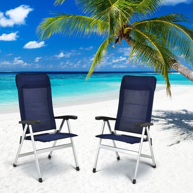 Two outdoor chaise lounges placed on a sandy beach with a palm tree and blue ocean in the background