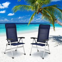 Two outdoor chaise lounges placed on a sandy beach with a palm tree and blue ocean in the background