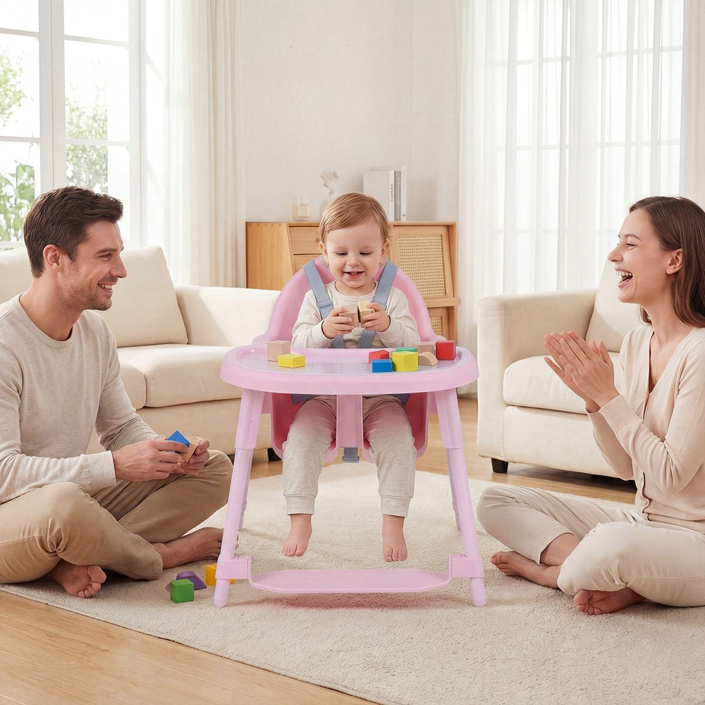 A family on the floor with a baby in the pink high chair, the parents are smiling and playing