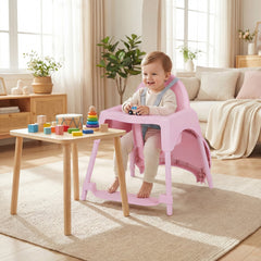 A happy baby sitting in the pink convertible high chair at a low wooden table, playing with toys