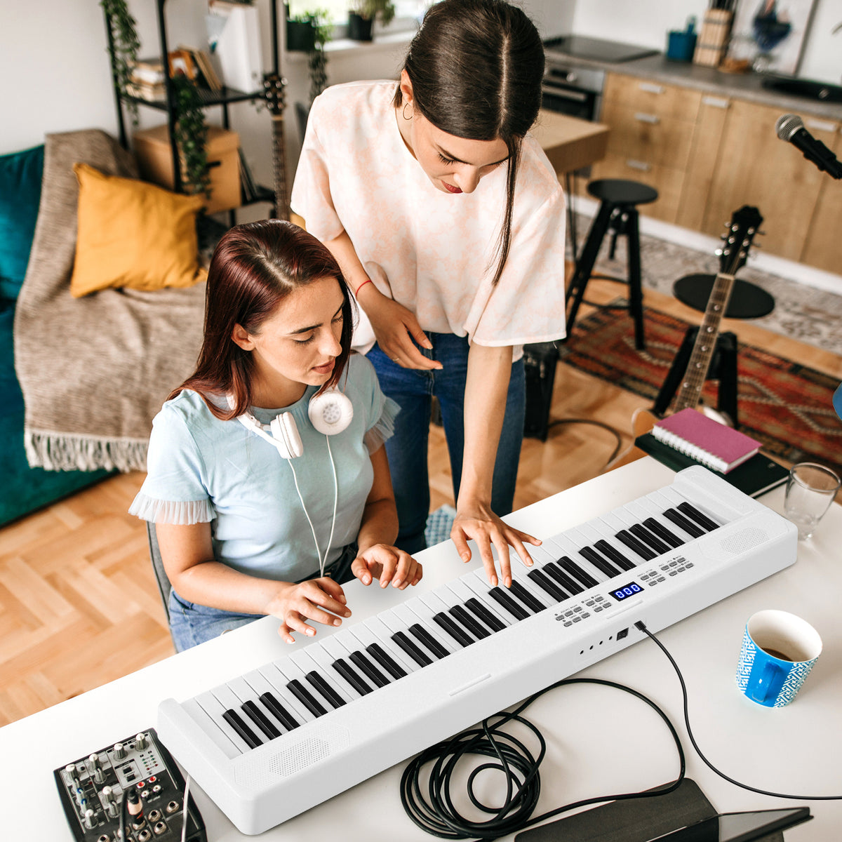 Two women playing the electronic keyboard in a bright room with musical instruments in the background