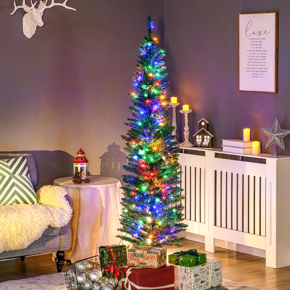 The artificial Christmas tree is lit up and decorated with presents underneath in a cosy room setting