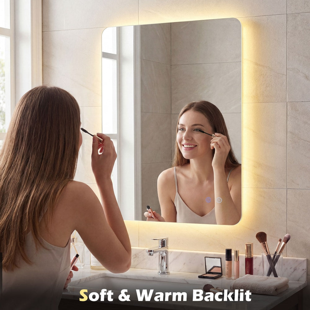 A woman applies mascara while looking into the lighted mirror, which has a soft warm backlight