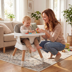 A woman plays with a baby sitting in the grey convertible high chair on a rug