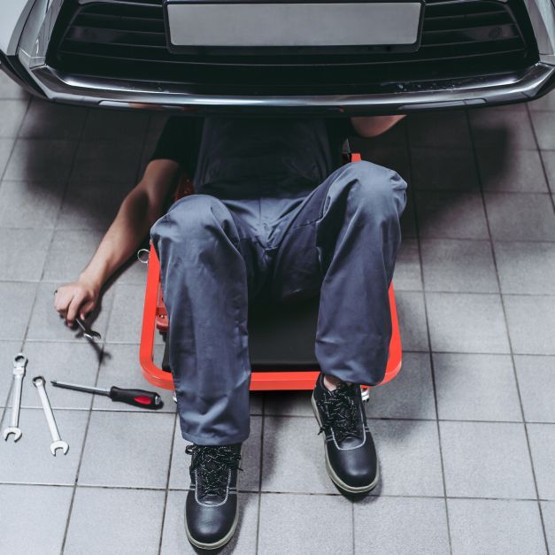 Mechanic lying on the creeper seat under a car with tools around