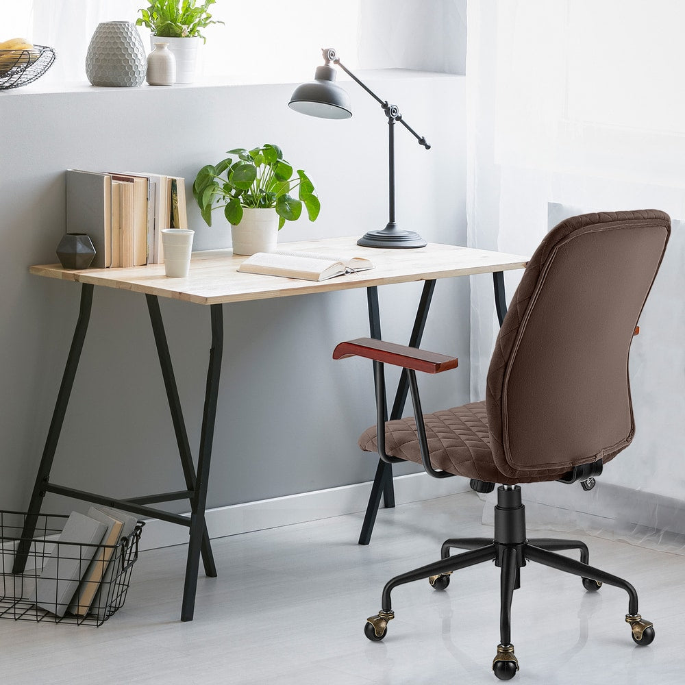 The office chair positioned at a wooden desk with a lamp and books in a bright room
