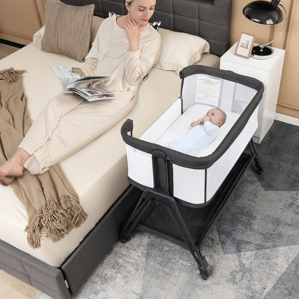 The bedside sleeper next to a bed with a baby inside and a woman reading