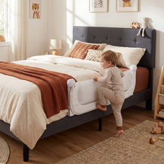 The bed rail secured to a grey upholstered bed as a toddler climbs into bed