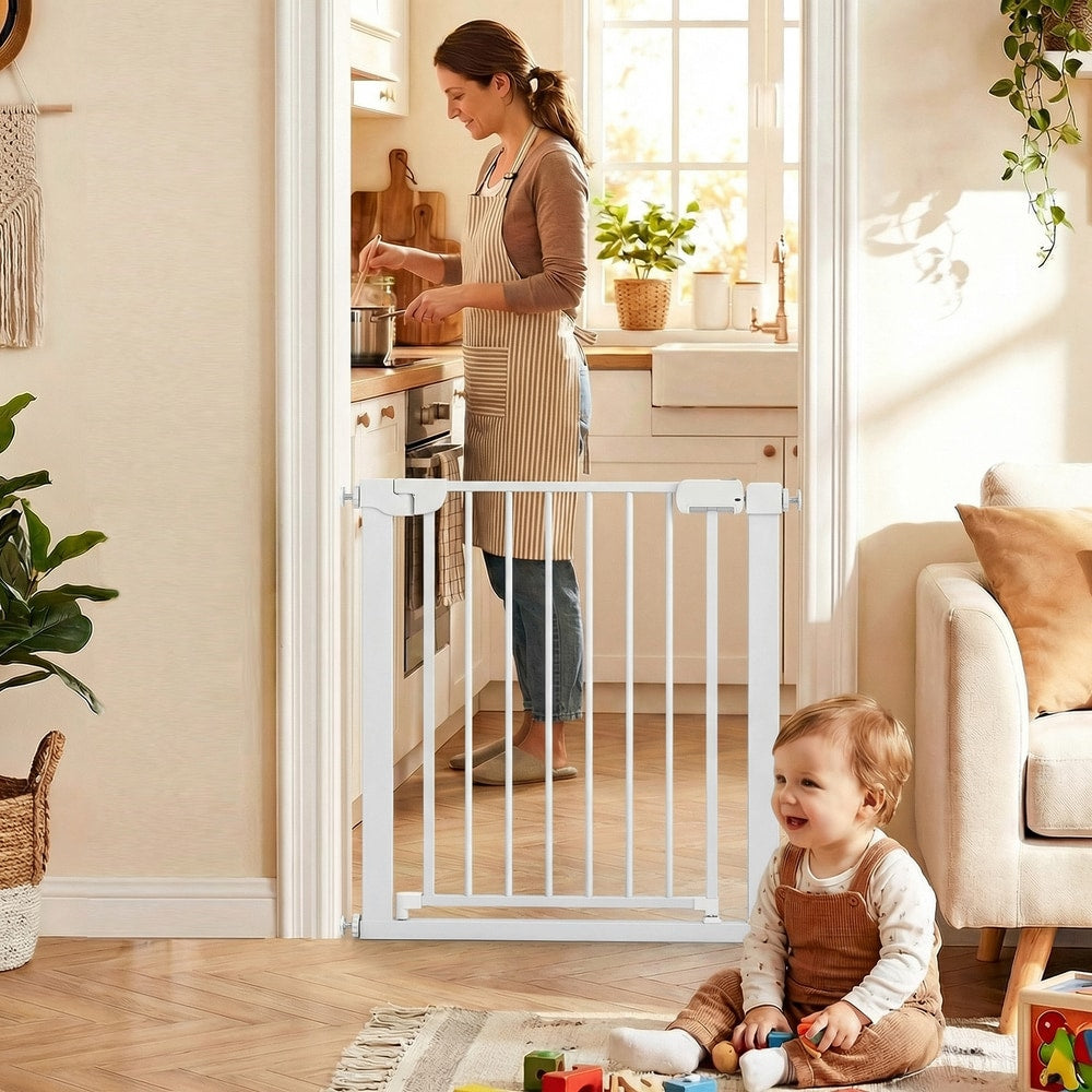 The pet gate positioned in a kitchen doorway while a baby plays on the floor in the foreground