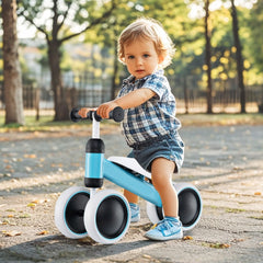 A happy toddler sits on the blue balance bike outdoors on a paved path