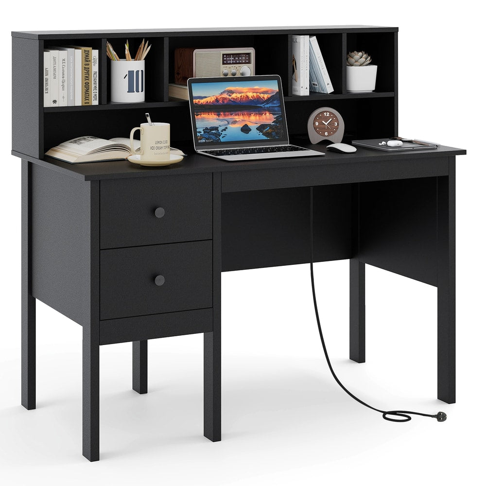 A black office desk with a laptop, books, and a mug, showing the power cord and charging station