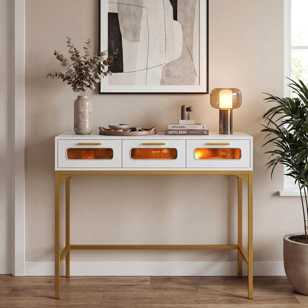 White console table with gold legs and three drawers, lit by a lamp