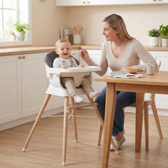 The high chair in use with a baby being fed by a woman in a bright kitchen setting