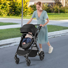 Woman pushing a black baby stroller with a baby sitting in the seat outdoors on a pavement