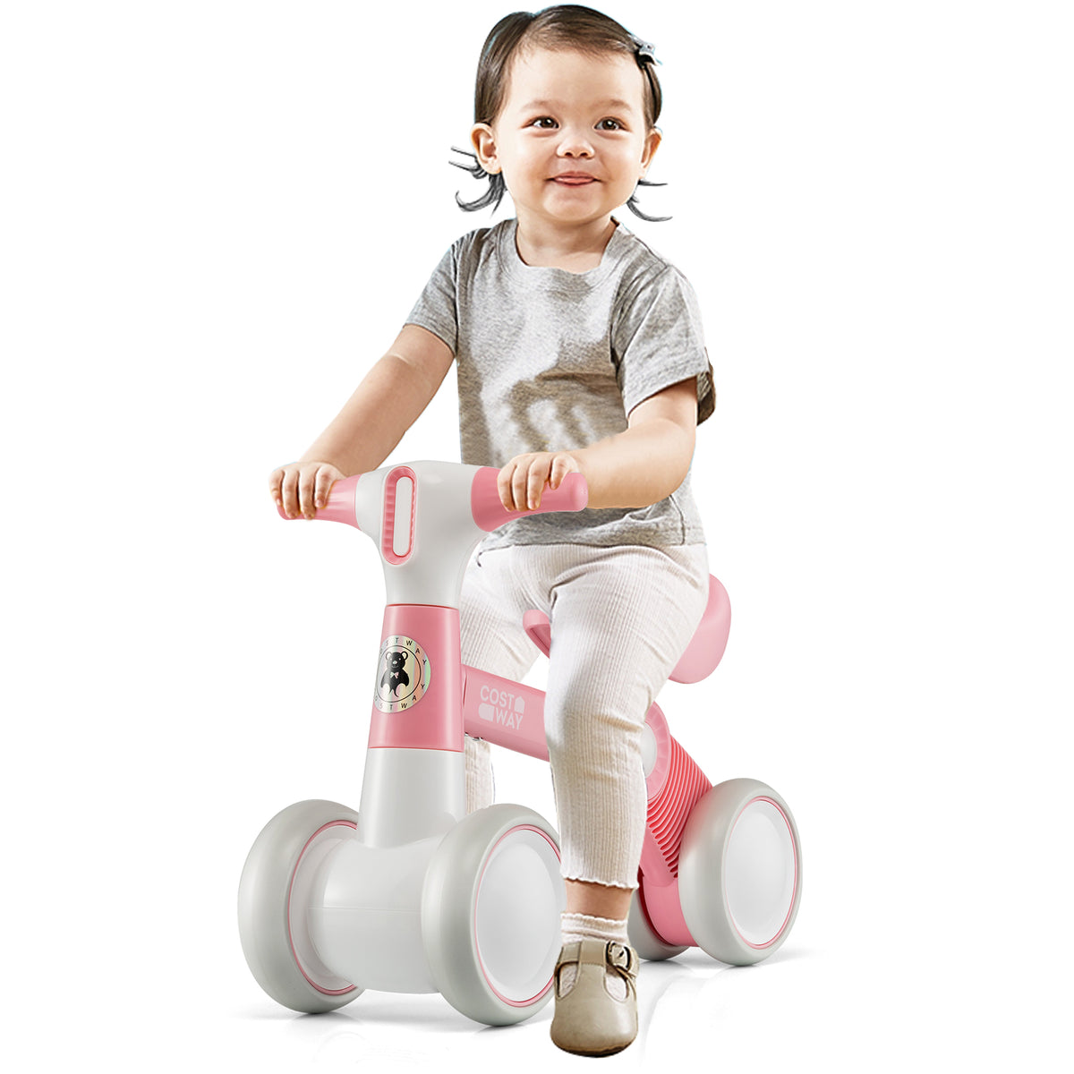 A baby sits on the pink balance bike, smiling at the camera