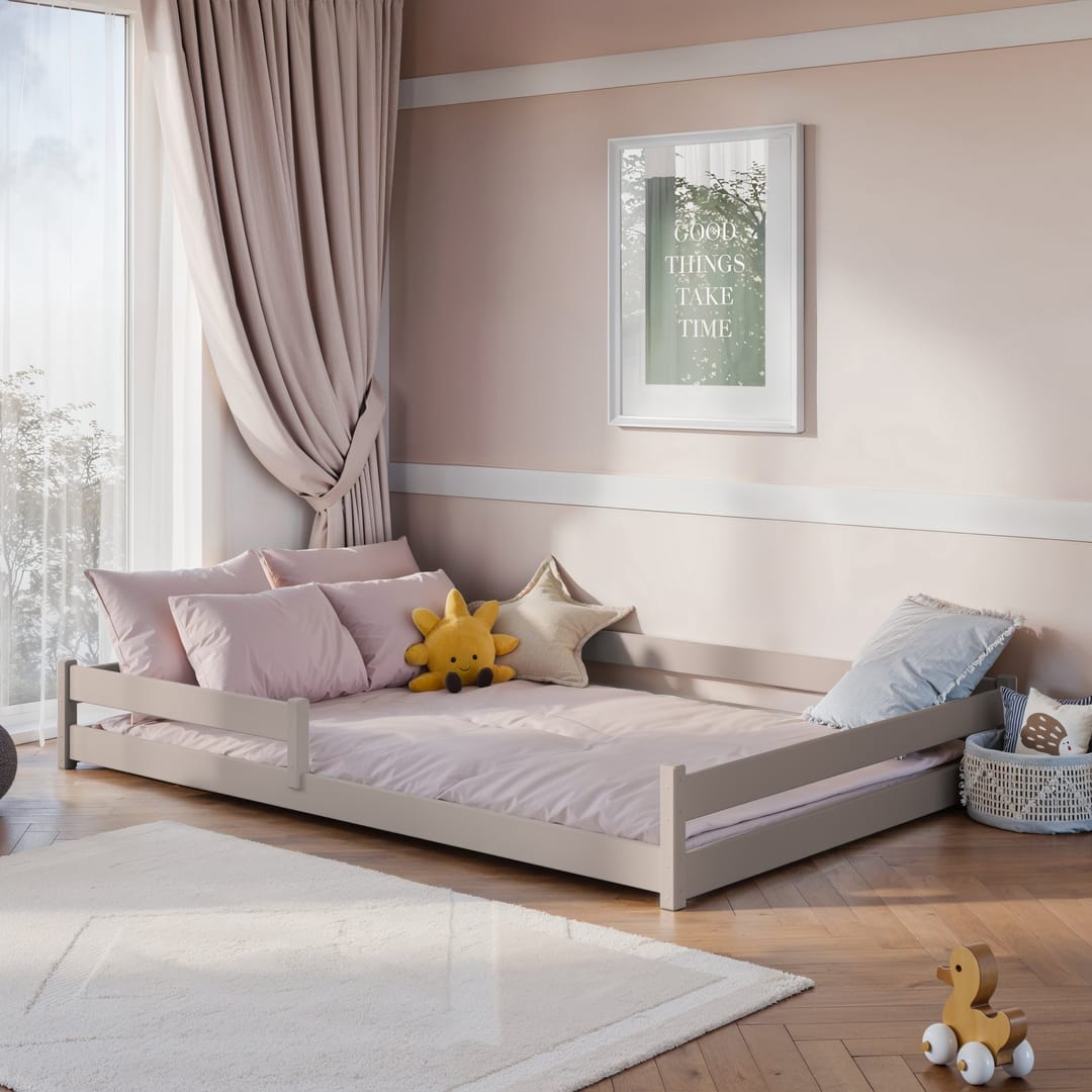 The light grey wooden bed frame in a child's bedroom with pink bedding and cushions