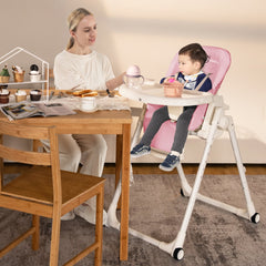 A woman feeding a baby in the pink high chair at a wooden table