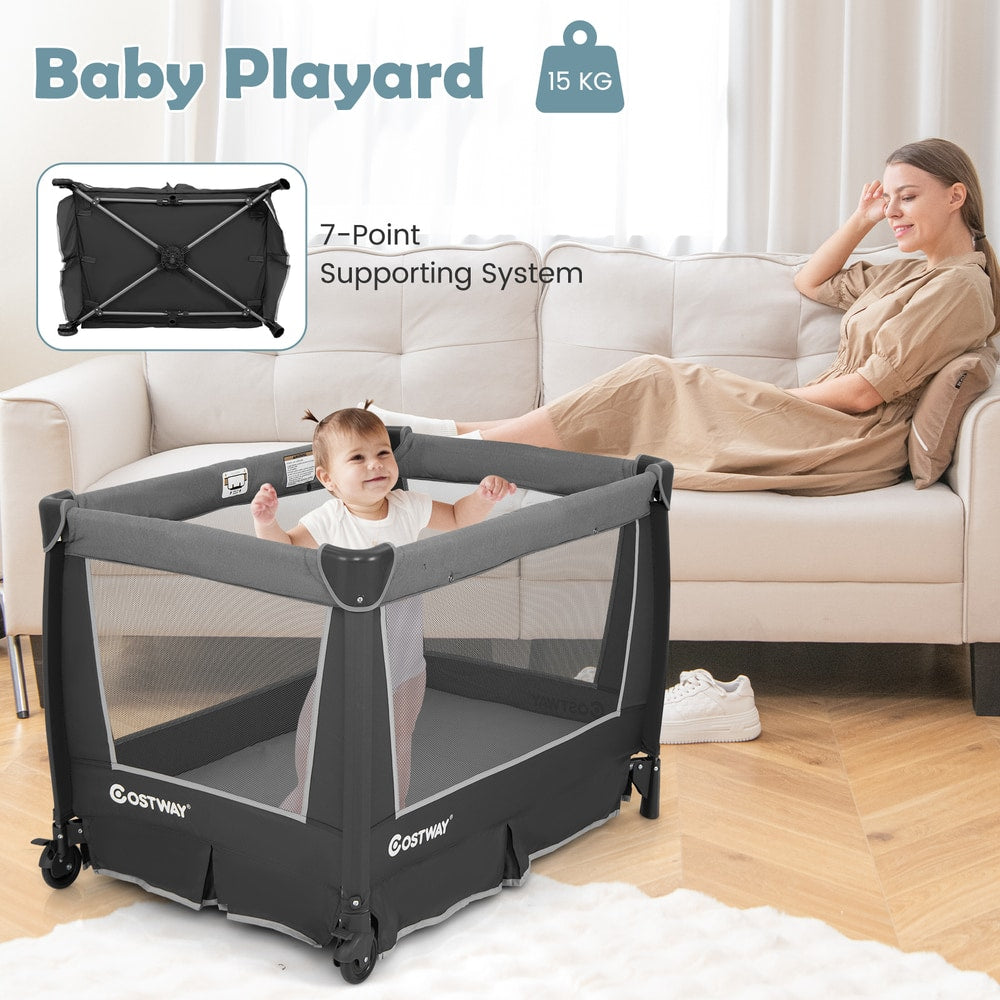 Baby playing inside the grey foldable pack and play with removable bassinet, set up in a living room