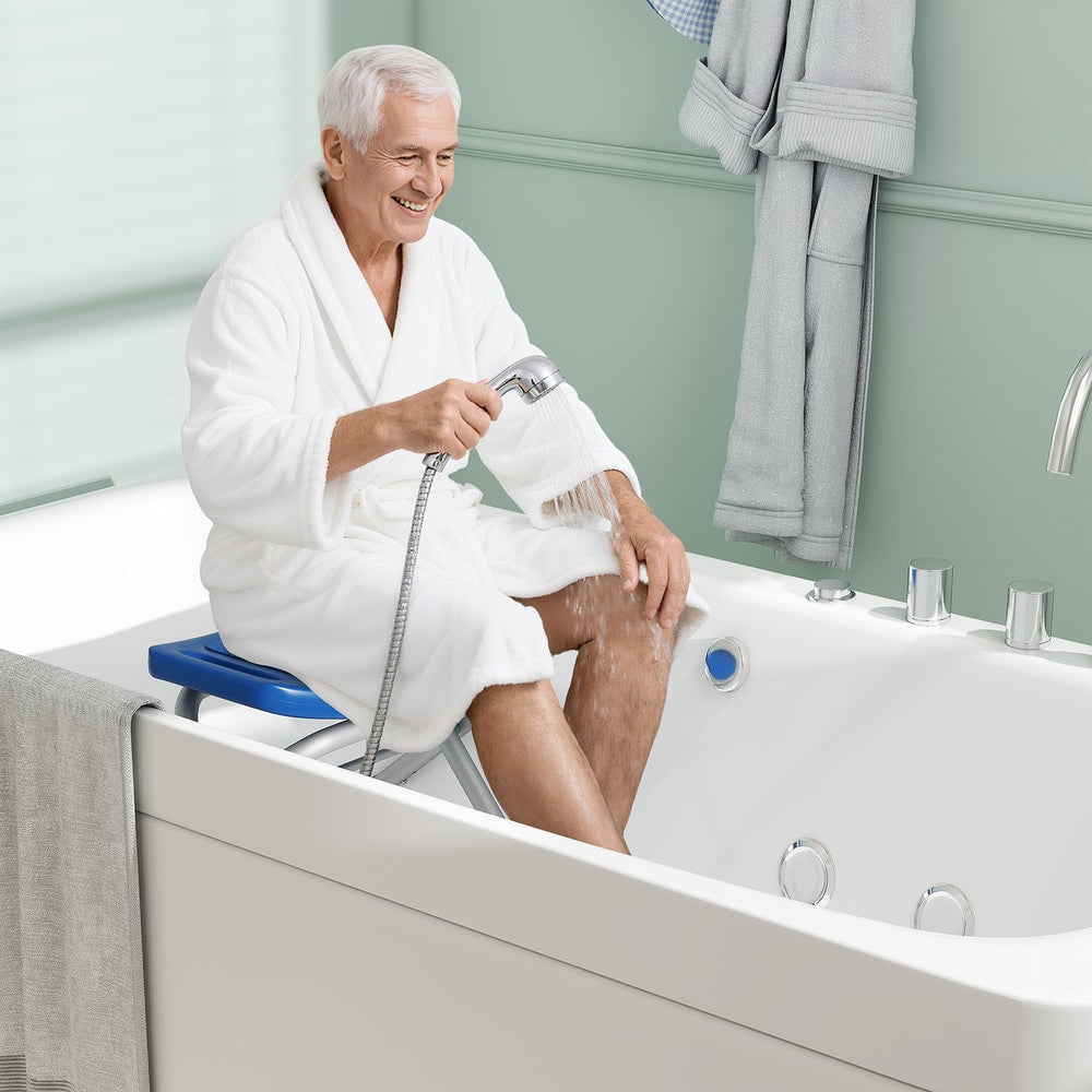 An elderly man sits on the blue bath safety seat in a bathtub holding a shower head