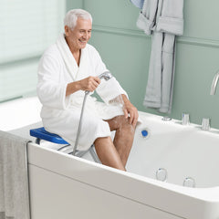 An elderly man sits on the blue bath safety seat in a bathtub holding a shower head