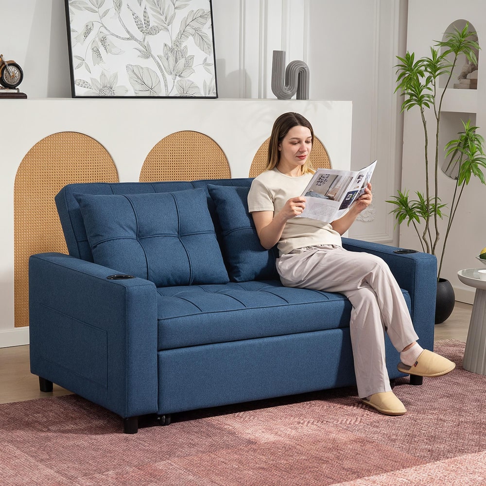 A woman reading a book on the dark blue two-seater sofa bed in a living room
