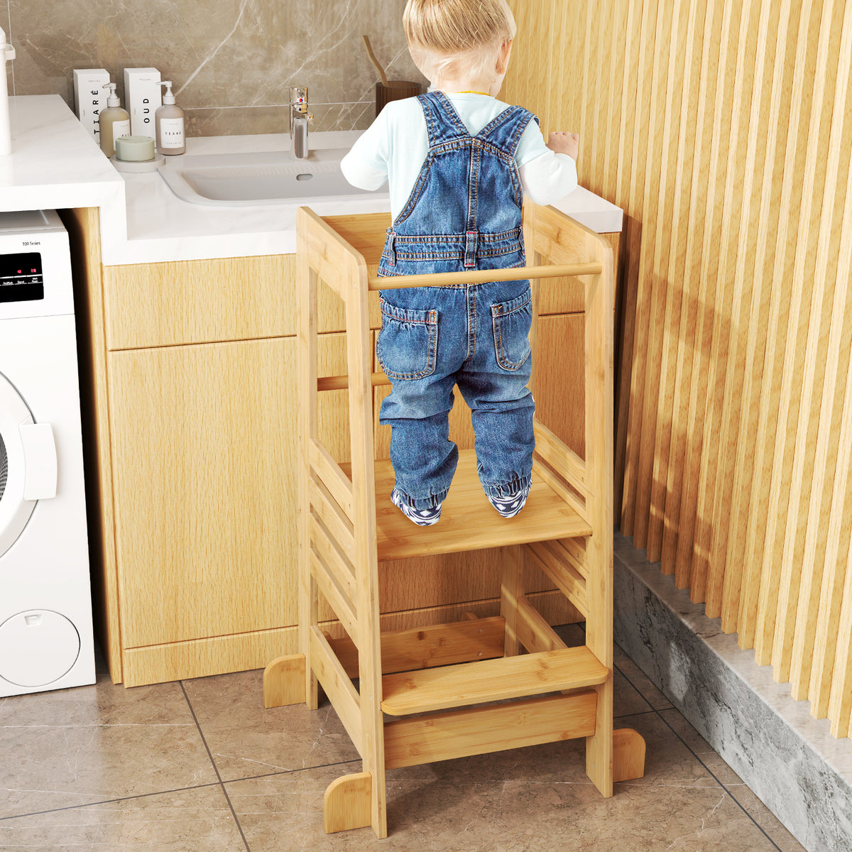 Child in dungarees using the step stool by a sink