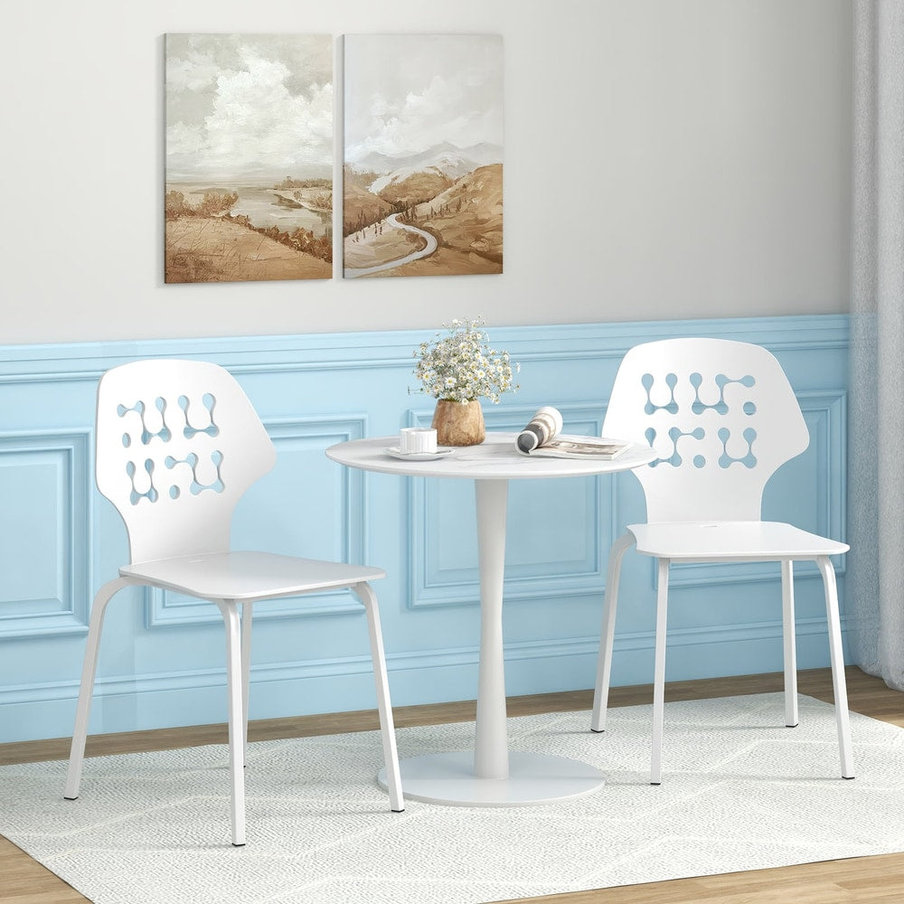 Two white metal dining chairs beside a small round table in a room