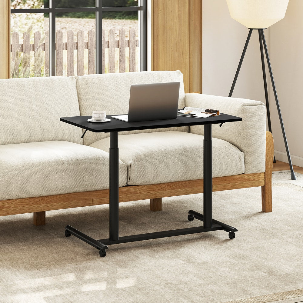 The office desk positioned in front of a sofa with a laptop and a cup of tea on the surface