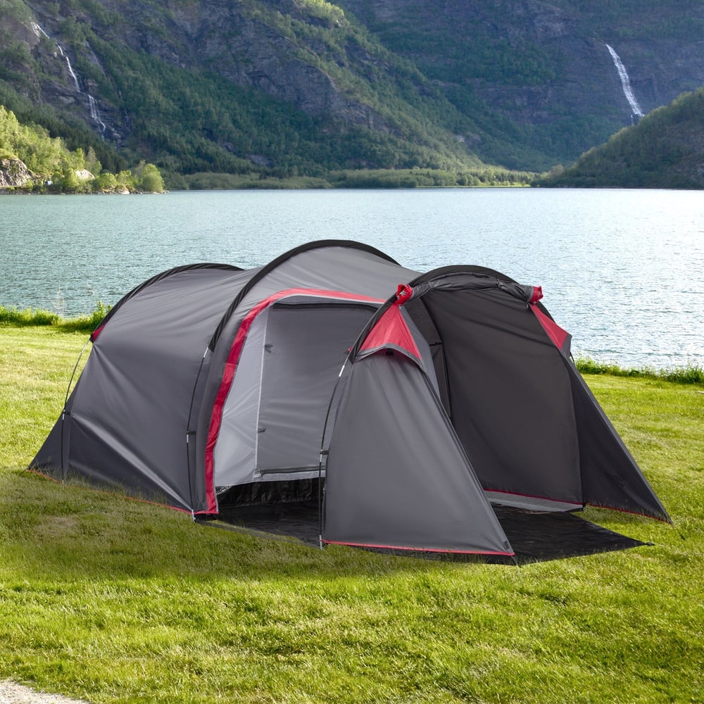 The grey camping tent is set up on a grassy area next to a body of water with hills in the background