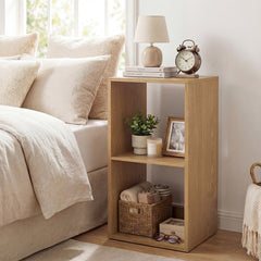 The natural wood open back 2-tier bookshelf standing next to a bed with a lamp and books on top