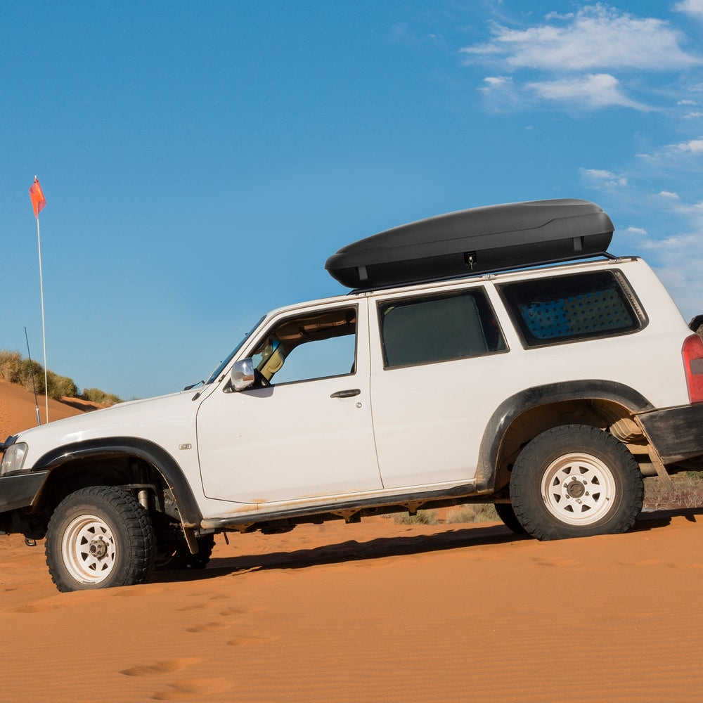 The rooftop cargo carrier mounted on a white car driving on sand dunes