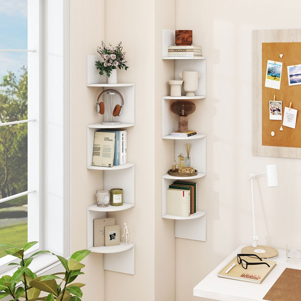 Two white corner shelves in a room with books and plants on them