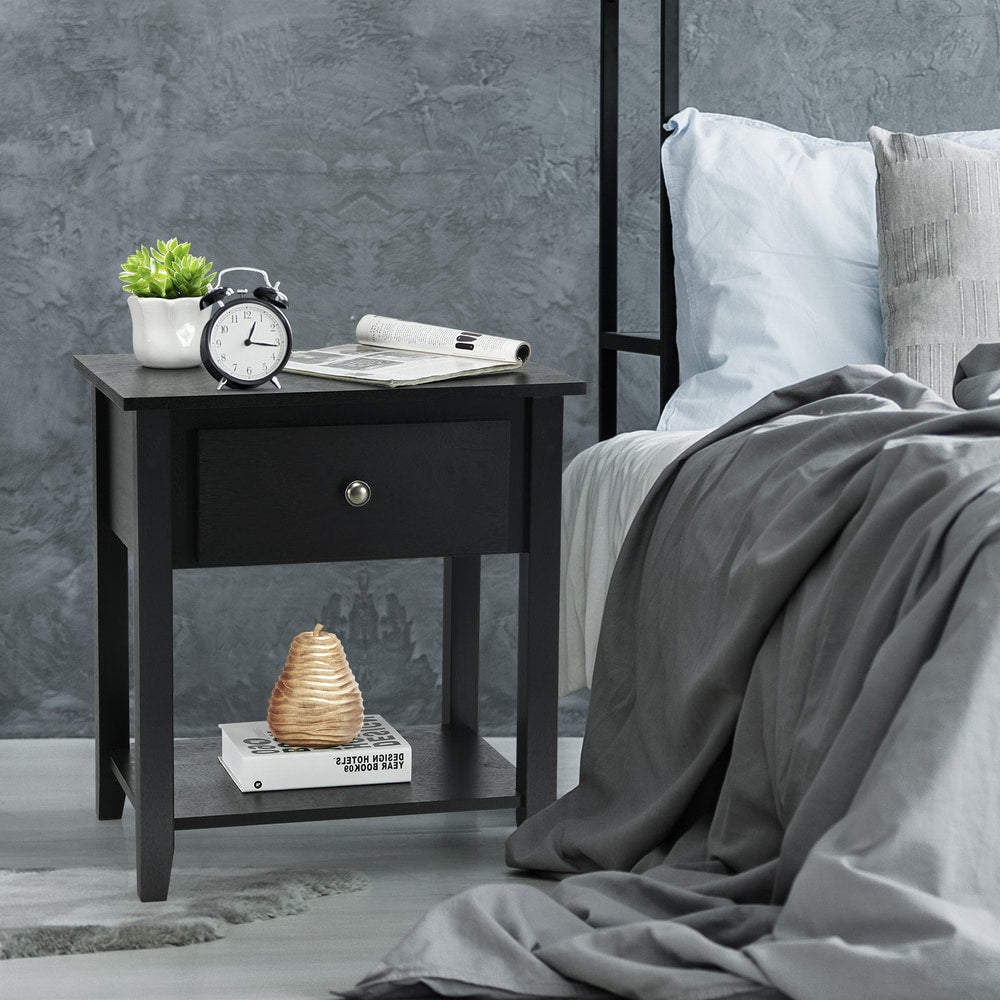The black side table used as a bedside unit with an alarm clock and books on the surface