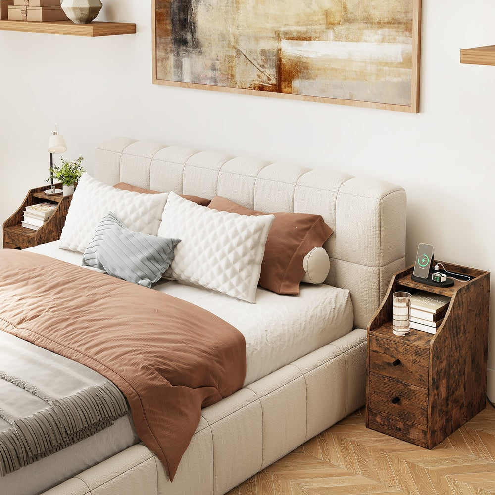 Two rustic brown end tables in a bedroom next to a bed, one with a phone charging