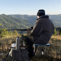 Man sitting on a blue folding stool hunting in the hills