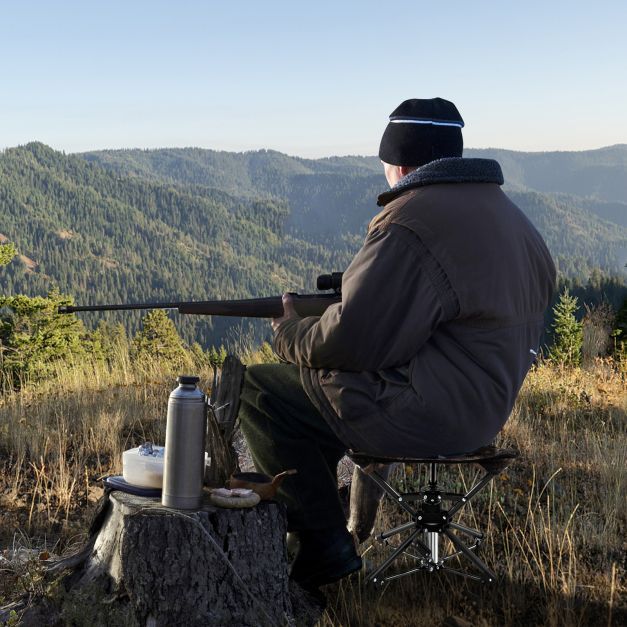 The camping stool in use by a hunter sitting on a tree stump in a mountainous landscape