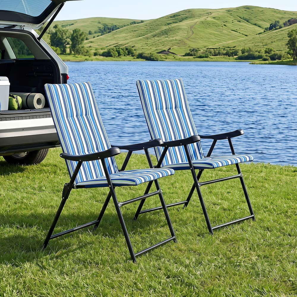 Two blue striped beach chairs on grass by a lake