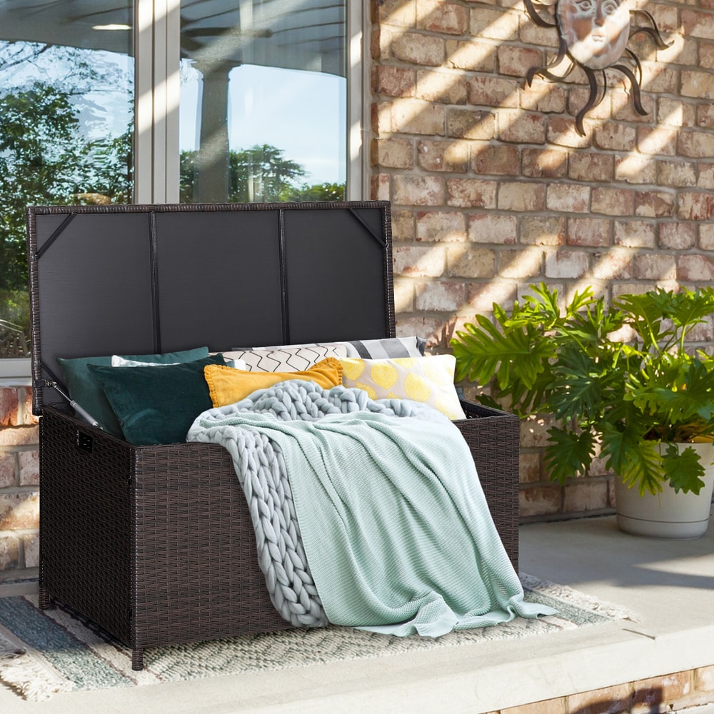 The deck storage box filled with cushions and blankets on a patio next to a brick wall