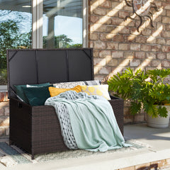 The deck storage box filled with cushions and blankets on a patio next to a brick wall