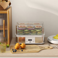 The food dehydrator on a kitchen counter, surrounded by fresh fruit and a drink
