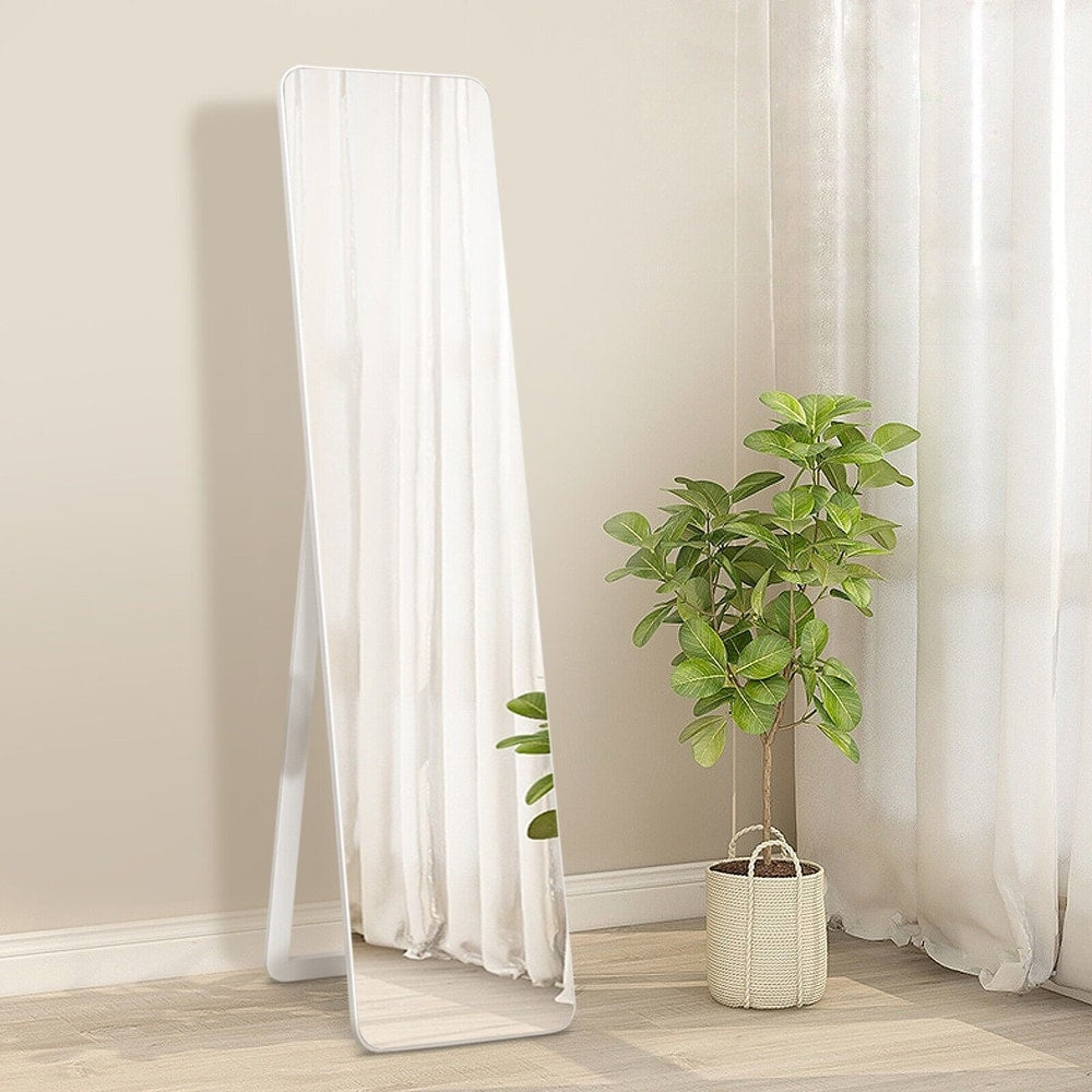 The white free-standing mirror placed in a room with plants and sheer curtains